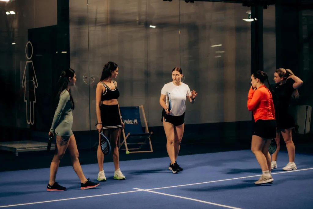 Four players during a padel doubles match on a glass-walled court
