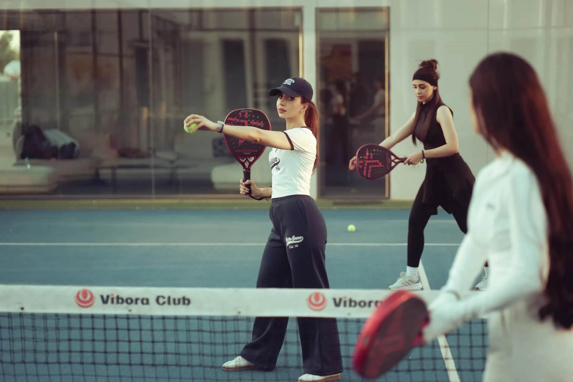 Padel players on an enclosed court with solid perforated rackets
