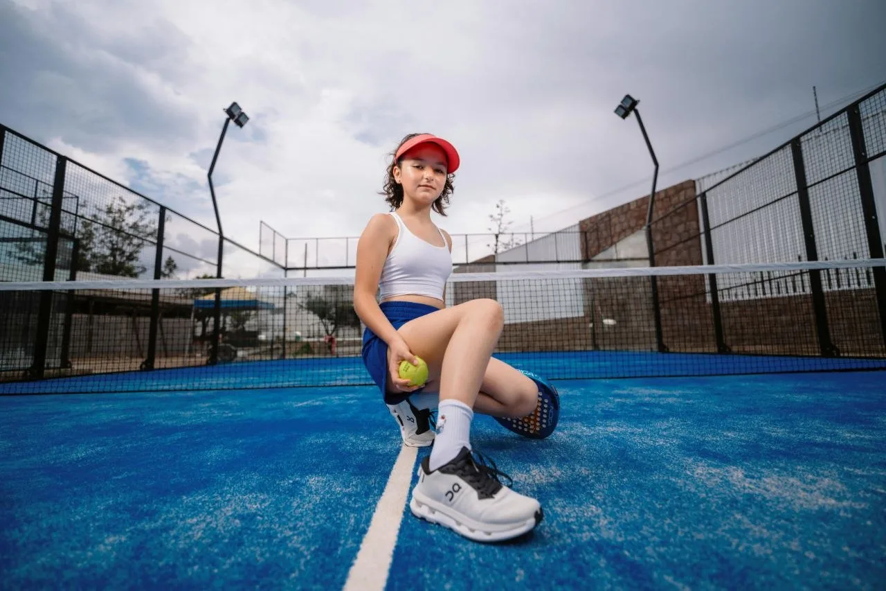 Young padel player sitting on a blue padel court with glass walls and floodlights