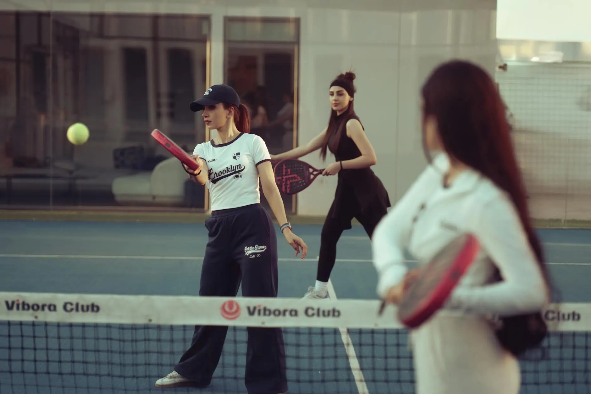 Players on a padel court with glass back wall clearly visible