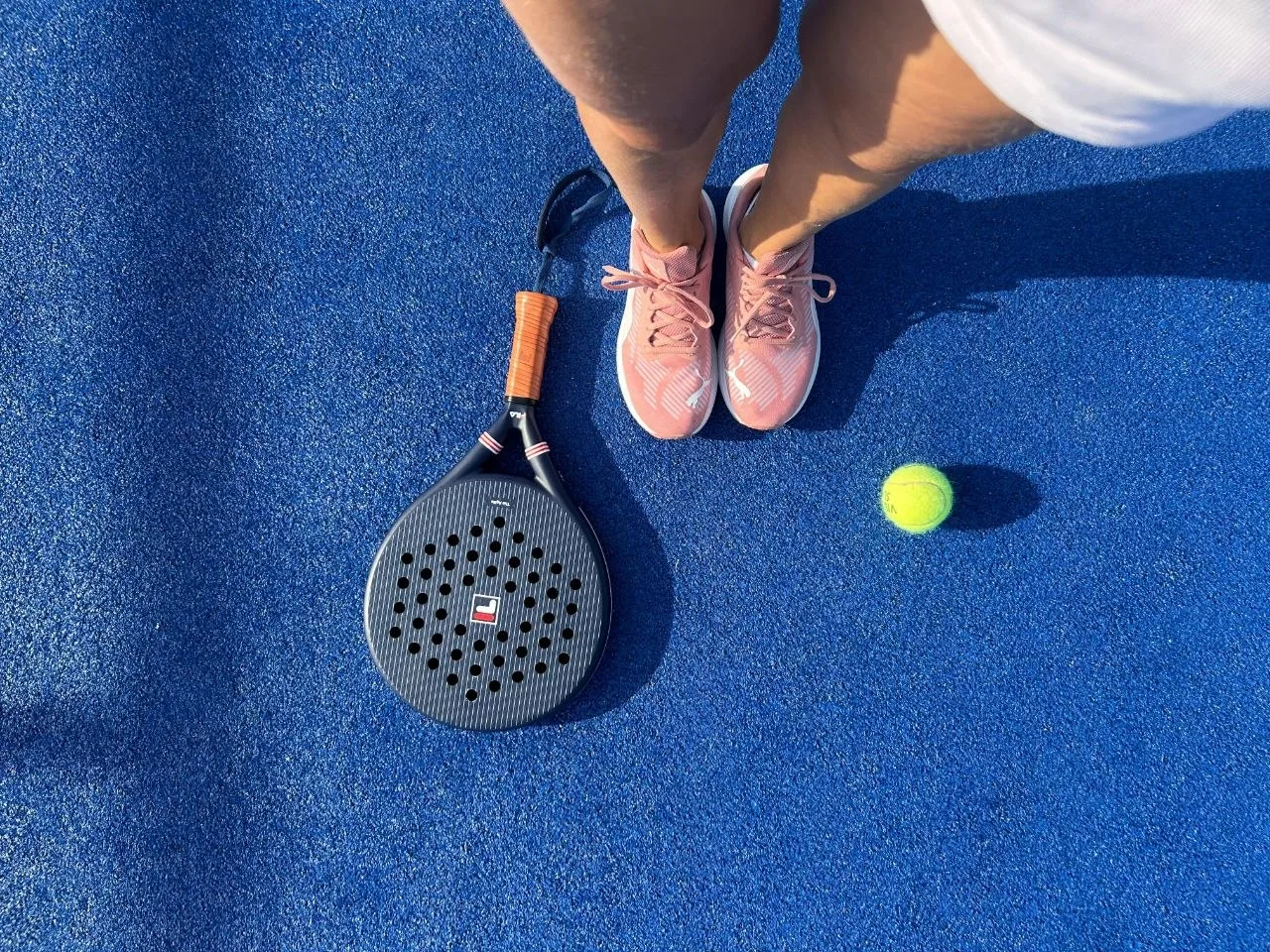 Padel shoes with racket and ball on blue artificial turf