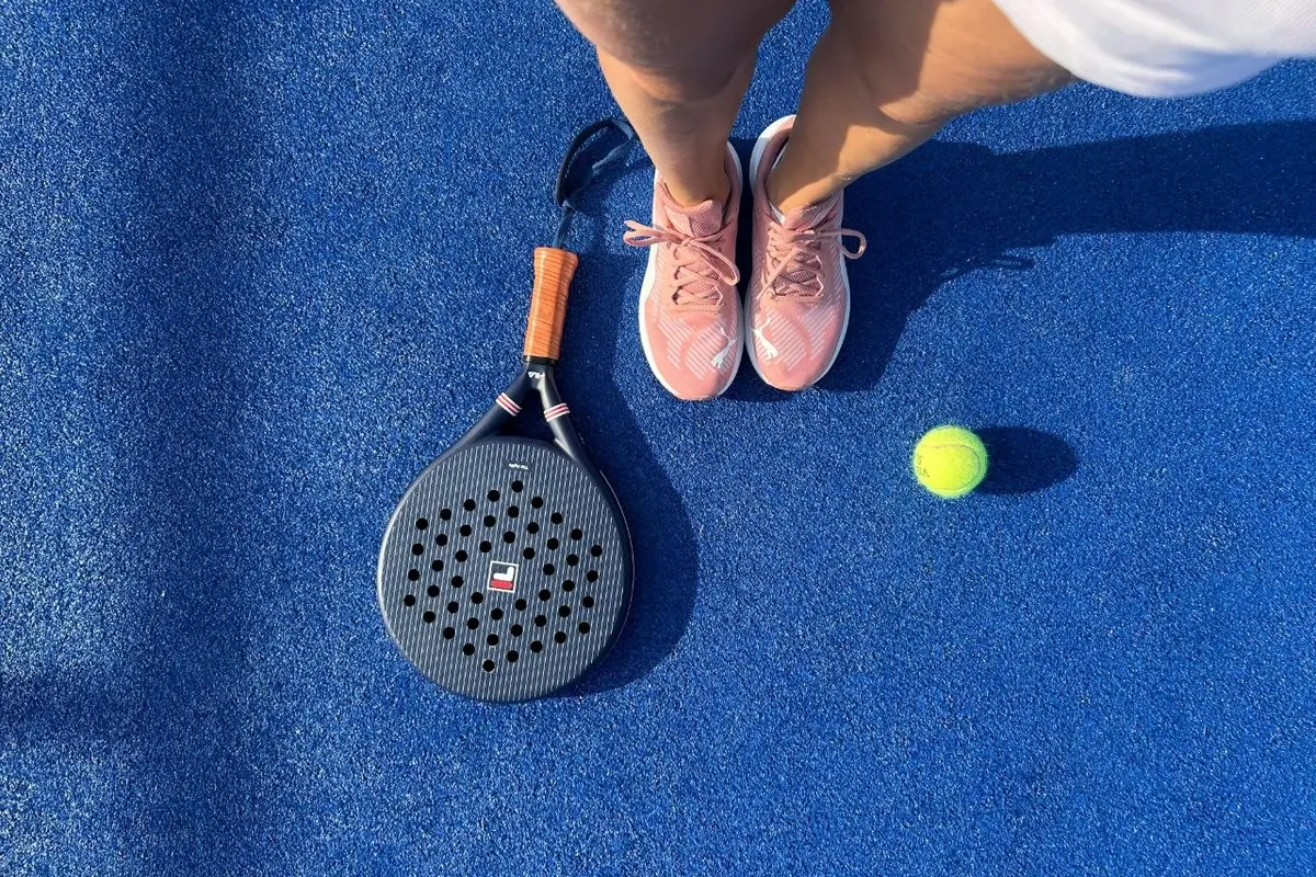 Padel racket, shoes and ball on a blue padel court surface